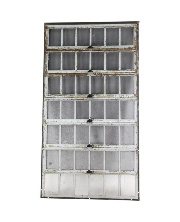 Industrial encasement window with a heavy steel frame and seven hinged sections of textured glass panes, shown full length with visible wear and some cracked panes.