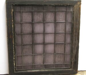 Wood-framed purple glass window with a grid of small textured panes and visible wear on the frame.