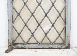 Steel framed leaded glass casement window with crisscross lites and a chipped, weathered frame.