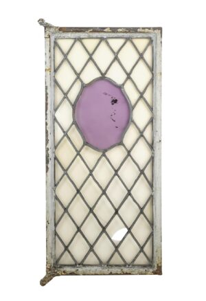 Steel framed casement window with leaded crisscross glass and a center purple shield-shaped panel, shown with weathered white-painted frame and visible damage along the edges.