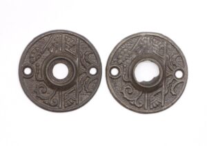 Pair of ornate cast iron door rosettes with a black finish, shown side by side, one with minor damage on the inner opening.