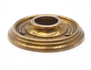 Close-up of a vintage cast brass concentric door rosette with a central opening and layered circular ridges in antique brass finish.