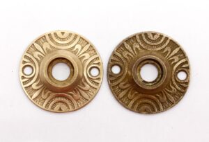 Pair of ornate bronze door rosettes shown as a pair, one with a polished finish and one with an antique finish, each with a central hole and two side mounting holes.