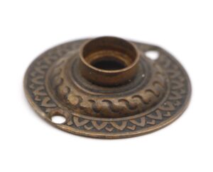 Antique brass door rosette with a radial patterned face and a raised center opening.