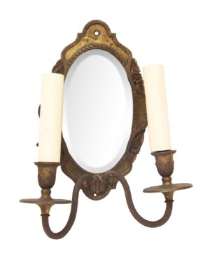 Victorian-style double arm wall sconce with an oval beveled mirror inset and two candle holders in an antique brass finish.