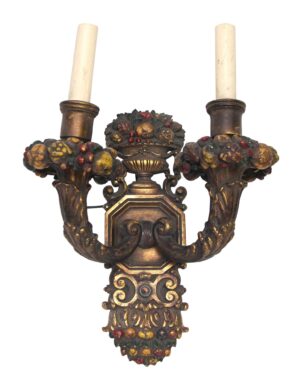 Gothic bronze wall sconce with two candle-style arms, ornate leaf and scroll details, and multi-colored decorative accents.