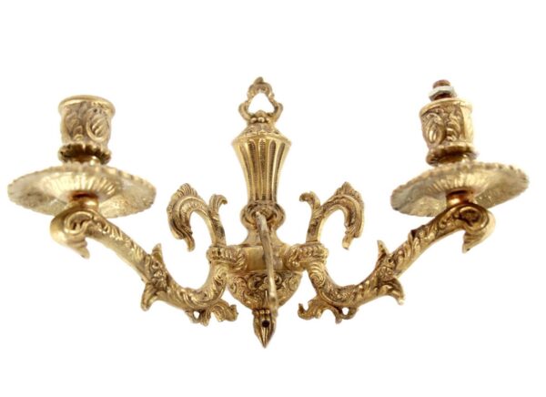 Ornate brass two-arm wall sconce with decorative scroll arms and candle-style holders.