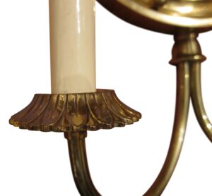 Close-up of a brass wall sconce showing one candle arm, a round frame edge, and a decorative scalloped base.