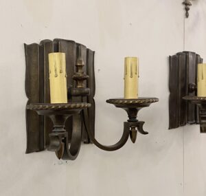 Traditional bronze two-arm wall sconce with an antique finish and candle-style holders.