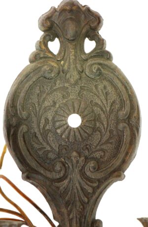 Ornate cast metal wall sconce backplate with a central opening and decorative scrollwork, shown in a close-up view.