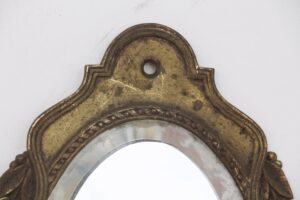 Close-up of an antique brass wall sconce with a beveled mirror inset and a mounting hole at the top.