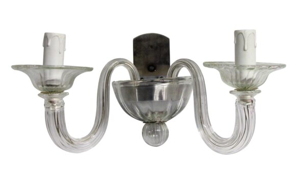 Clear glass double-arm wall sconce with a vertical metal back plate and two candle-style bulb holders.
