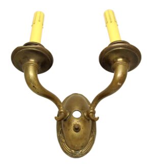 Antique bronze two-arm wall sconce with curved arms and candle-style bulb sleeves, shown front view on a decorative backplate.