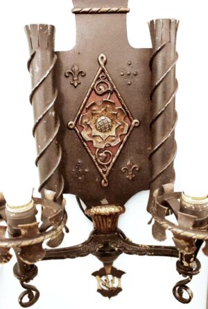 Pair of Tudor-style two-arm wall sconces with ornate bronze and wrought iron details, shown in a close-up of one sconce body and arms.