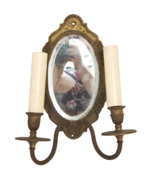 Victorian wall sconce with two arms, an oval beveled mirror inset, and an antique brass finish.