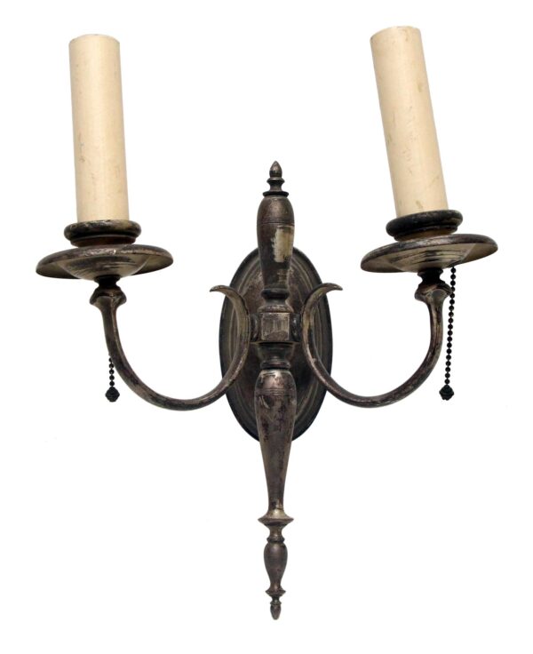 Neoclassical wall sconce with two slender arms, candle cups, and a distressed silver finish.
