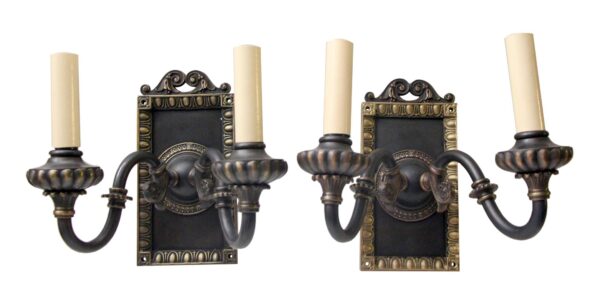 Pair of Tudor wall sconces with two candle-style lights each, shown as a matching set with ornate black and gold metal backplates and curved arms.