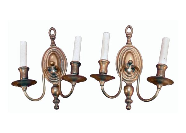 Pair of colonial copper two-arm wall sconces shown as a matching pair, each with two candle-style arms and an oval backplate.