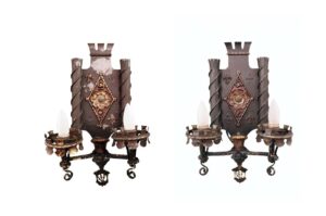 Pair of Tudor-style wall sconces shown side by side, each with two arms, ornate details, and candle-style bulbs in an antique bronze and black finish.