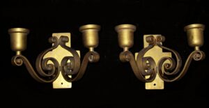 Pair of bronze wall sconces with two decorative curly arms and candle-style cups, shown as a matching pair.