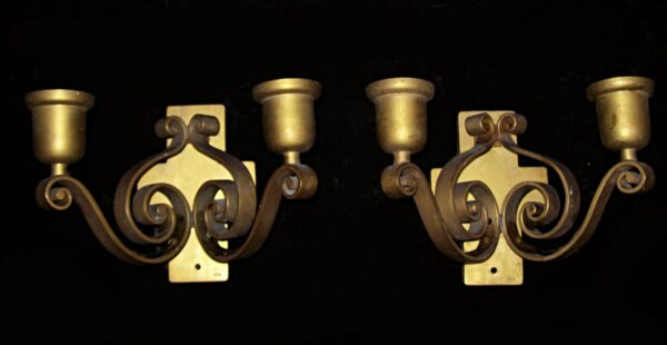 Pair of bronze wall sconces with two decorative curly arms and candle-style cups, shown as a matching pair.