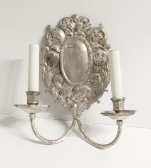Pair of Louis XV rococo wall sconces with ornate floral and foliage detail, two candle-style arms, and visible wear on the silvered finish.