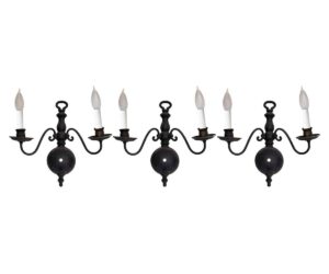 Set of three colonial wall sconces with two arms each, shown in a black finish and fitted with candle sleeves.