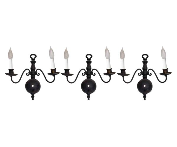Set of three colonial wall sconces with two arms each, shown in a black finish and fitted with candle sleeves.