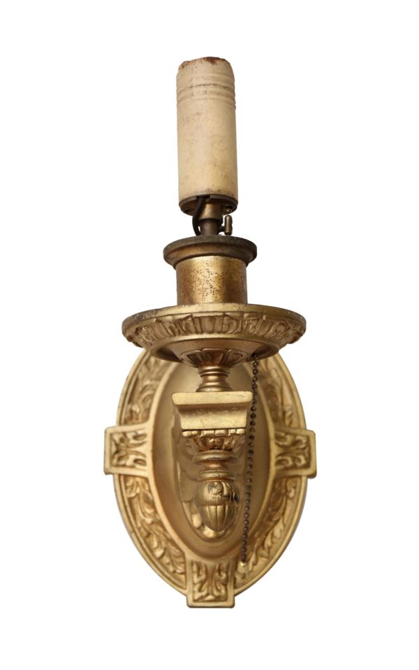 Victorian-style wall sconce with an ornate oval brass backplate, a single candle-style socket, and a pull chain visible on the right.