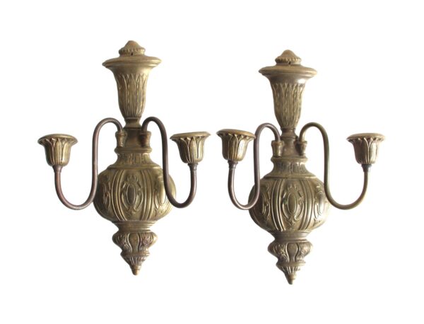 Pair of cast brass wall sconces with two curved arms and decorative urn-shaped bodies, shown front view with an antique brass finish.