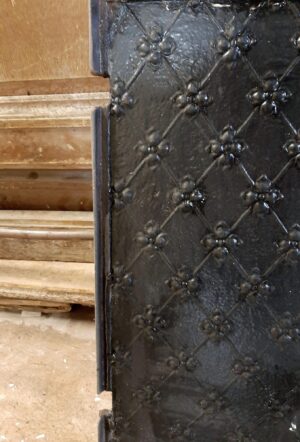 Close-up of a black cast iron fire back with a fleur de lis pattern and raised diamond lattice detail.