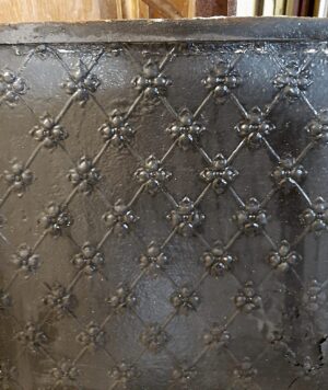 Close-up of a black cast iron fire back centerpiece with a diamond lattice and fleur de lis detail.