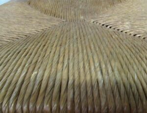 Close-up of a hand-caned chair seat in a light wood tone, showing the woven surface and seat edge.