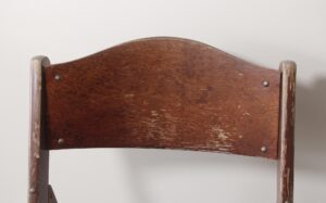 Close-up of the curved wood backrest and side supports on a folding chair with visible wear.