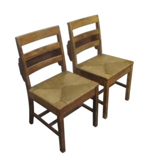 Pair of antique schoolhouse chairs with square wooden backs and woven seats, shown at a slight angle.
