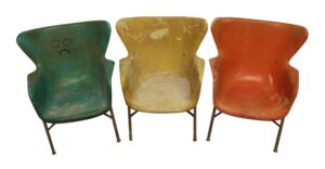 Three fiberglass chairs in green, yellow, and orange, each with metal legs and a worn, weathered look.
