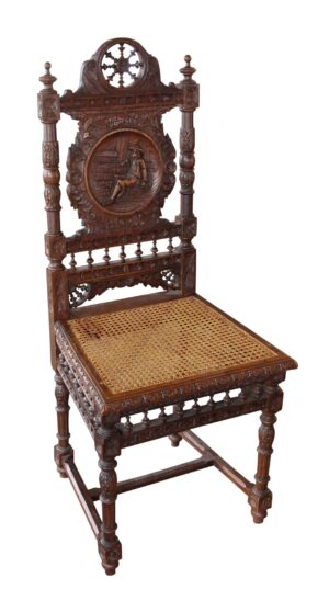 An English Renaissance carved wooden chair in dark wood tone with a wicker seat and an ornate figural backrest.