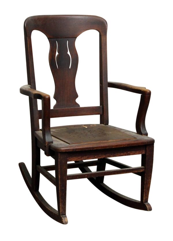 A dark wood rocking chair with worn wooden arms, a carved back panel, and visible age marks on the seat and frame.