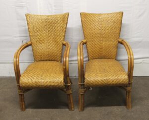 Pair of vintage tan wicker chairs with wooden frames, shown side by side, each with a high back, curved armrests, and visible wear.