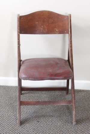 Vintage folding chair with a bentwood back, dark wood frame, and a worn red vinyl seat cushion.