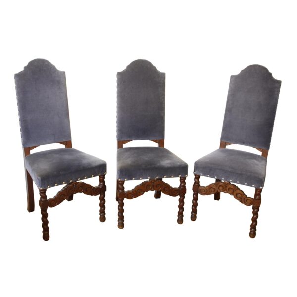 Three high-back chairs with blue upholstered seats and backs, brass nailhead trim, and carved dark wood legs and front stretchers, shown from slightly different angles.