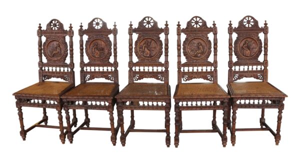 Set of six carved wooden chairs with wicker seats, shown front view, each back featuring a different figural relief and one seat with visible damage.