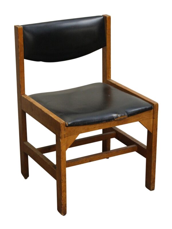 Mid-century wooden chair with black vinyl seat and back, shown in a three-quarter view with visible age wear on the front edge of the seat.