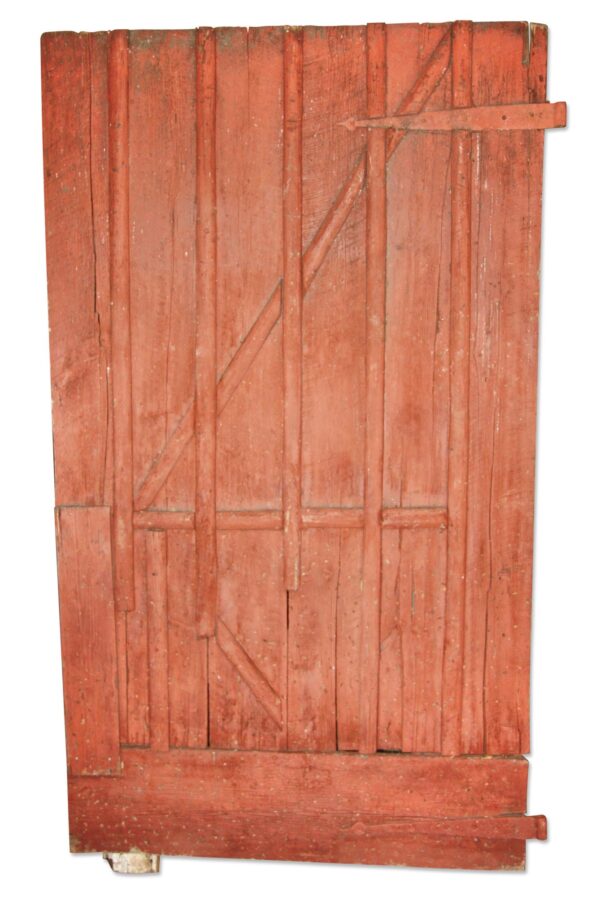 Antique red painted wooden barn door with distressed vertical boards and diagonal bracing, shown full length with original strap hinge pieces still attached.