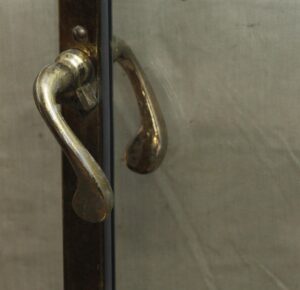 Close-up of a brass shower door lever handle and frame beside clear glass.