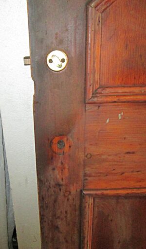 Close-up of a dark wood tone five-panel door showing the latch edge and cracked molding near the bottom.
