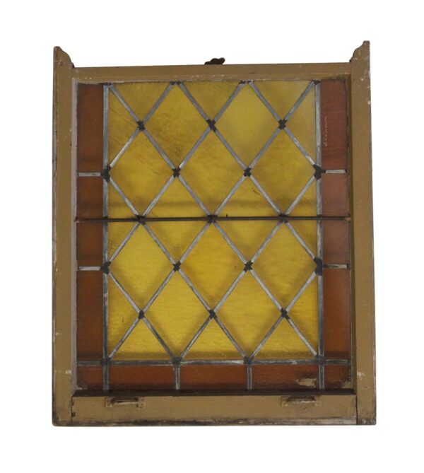 Antique stained glass window in a wood frame with amber and brown panes, a diamond leaded pattern, and visible wear along the edges.