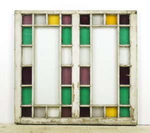 Antique Queen Anne stained glass window with a weathered white pine frame and intact multi-colored panes arranged in a geometric grid.