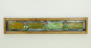 Art Nouveau stained glass window with a light wood pine frame and three repeating decorative motifs in a long horizontal panel.