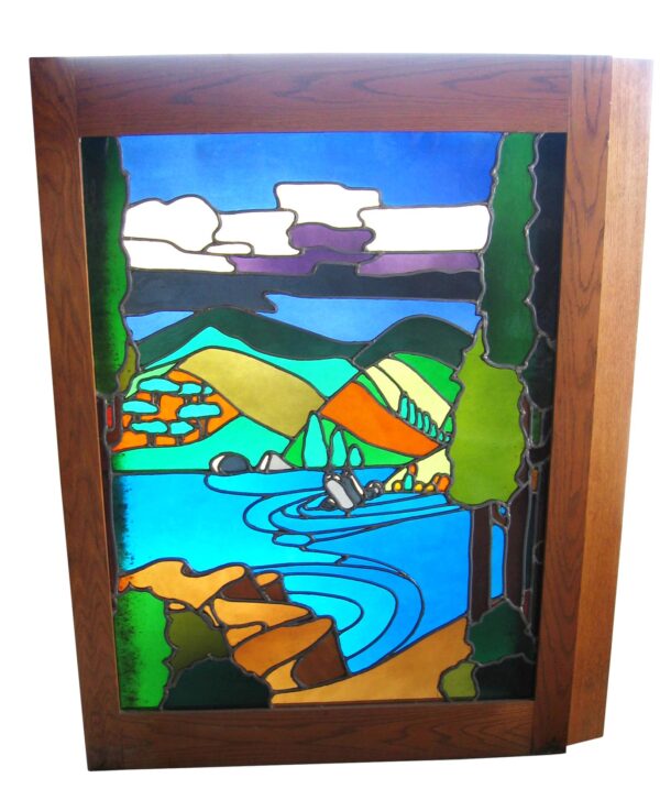 Backlit stained glass window in a dark wood tone frame, showing a colorful pastoral scene with hills, water, trees, and clouds.